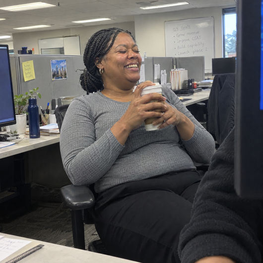 Woman laughing at her office desk, grey top smooth at the waist